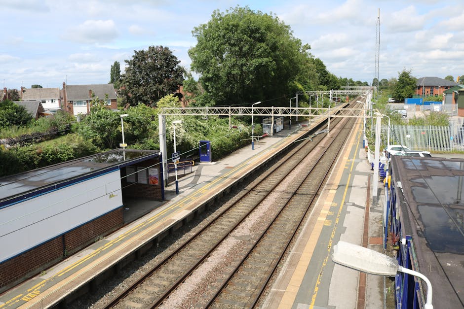A modern electric train with a sleek, aerodynamic design is stationed at a railway platform, ready for boarding. The train's exterior features a silver body with prominent red accents along the sides,